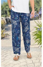 Locker sitzende, dunkelblaue Freizeithose mit abstraktem weißen und hellblauen Muster, elastischer Bund, gerade geschnitten, getragen von stehender Person mit weißen Sandalen und weißem T-Shirt