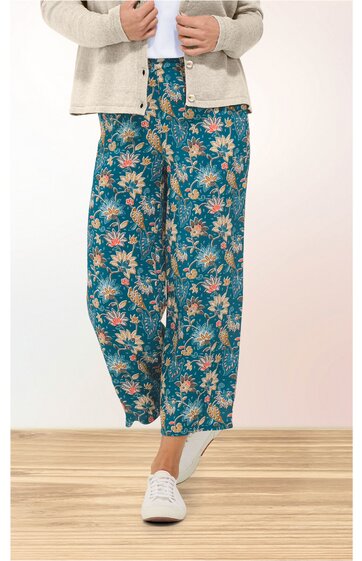 Weite Hose in petrolgrün mit Blumenmuster in Weiß und Orange, hoher Bund mit Gummizug, locker sitzend, getragen von stehender Person, kombiniert mit weißem Schuh und beigem Cardigan