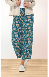 Weite Hose in petrolgrün mit Blumenmuster in Weiß und Orange, hoher Bund mit Gummizug, locker sitzend, getragen von stehender Person, kombiniert mit weißem Schuh und beigem Cardigan