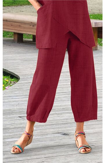 Rote weite Hose mit elastischem Saum am Beinabschluss, zwei seitliche Taschen, getragen von stehender Person, kombiniert mit bunten Sandalen mit Riemchen