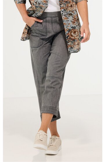 Graue, gerade geschnittene Damenhose mit Bündchen am Saum, schrägen Eingrifftaschen, getragen von stehender Person, kombiniert mit weißem Oberteil und langem, gemustertem Mantel, weiße Sneakers