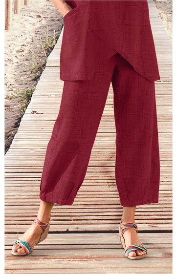 Weinrote, weite Stoffhose mit elastischem Saum am Beinabschluss, getragen von stehender Person, mittellang, mit lockerer Passform