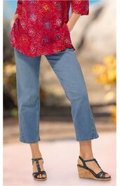 Jeanshose in Hellblau, gerade geschnitten, knöchellang, getragen von stehender Person, kombiniert mit roten, gemusterten Oberteil, schwarze Sandaletten mit Keilabsatz und Riemen