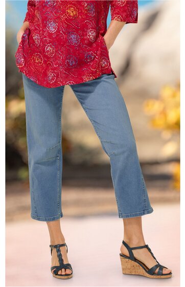 Jeanshose in Hellblau, gerade geschnitten, knöchellang, getragen von stehender Person, kombiniert mit roten, gemusterten Oberteil, schwarze Sandaletten mit Keilabsatz und Riemen