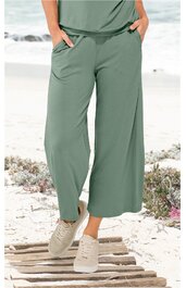 Hose in Salbeigrün, weit geschnitten, mit seitlichen Eingrifftaschen, elastischem Bund, getragen von stehender Person am Strand, knöchellang