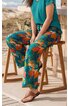 Weite, locker sitzende Hose mit farbigem Blumenmuster in Orange und Blau auf grünem Grund, getragen von sitzender Person, Kombiniert mit türkisem Kurzarmshirt und braunen Zehentrennern