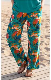 Freizeitlange Hose in Türkis mit buntem Blumen- und Blättermuster, weiter Beinverlauf, getragen von stehender Person mit grüner Oberbekleidung und braunen Sandalen, Taschen an den Seiten