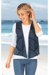 Dunkelblaue Weste mit schwarzen, abstrakten Mustern, offene Vorderseite ohne Verschluss, ärmellos, vorne schmal zulaufend, getragen von lächelnder Frau im Stehen, kombiniert mit weißem Langarmshirt und blauen Jeans