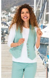 Hellgrüne Weste ohne Muster mit sechs silbernen Knöpfen, V-Ausschnitt, tailliert, getragen von lächelnder Frau mit lockigen roten Haaren, kombinierbar mit weißem langärmligem Shirt und hellgrüner Hose