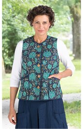 Ärmellose Weste in Dunkelblau mit grünem Blumenmuster, durchgehende Druckknöpfe vorne, Stehkragen, eine aufgesetzte Tasche rechts, getragen von Frau im Stehen, weißes 3/4-Armshirt darunter, dunkelblaue Hose mit Taschen