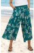 Weite, knöchellange Hose in Petrol mit großem weißen Blumenmuster, elastischer Bund, seitliche Eingrifftaschen, getragen von stehender Person am Strand