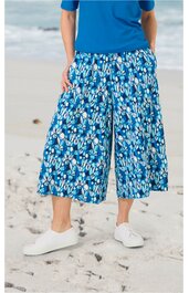 Hose in Capri-Länge, hellblau mit weißem und dunklem abstraktem Muster, locker sitzend, elastischer Bund, getragen von stehender Person am Strand, kombiniert mit blauem Oberteil und weißen Schuhen