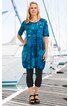 Türkis-blau gemustertes Kleid, knielang, kurze Ärmel, Rundhalsausschnitt, Seitentaschen, Taillenweite mit Tunnelzug, getragen von stehender Frau auf Steg vor Segelbooten, kombiniert mit schwarzen Caprileggings und schwarzen Sandalen