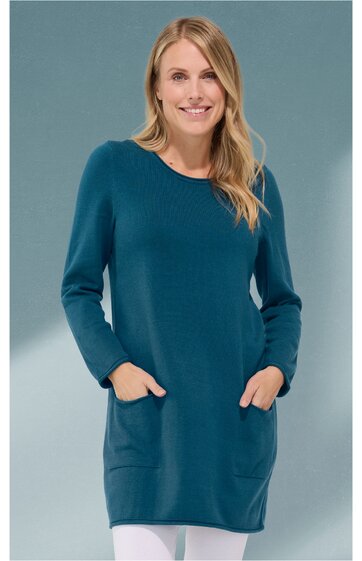 Langärmliges Kleid in petrolblau, ohne Muster, Rundhalsausschnitt, aufgesetzte Taschen vorne, gerade geschnitten, getragen von frontal stehender Frau mit Händen in den Taschen