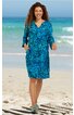 Blaues midikleid mit floralem muster, V-Ausschnitt, 3/4-ärmel mit Schlitz, seitliche taschen, gerade geschnitten, getragen von stehender frau am strand