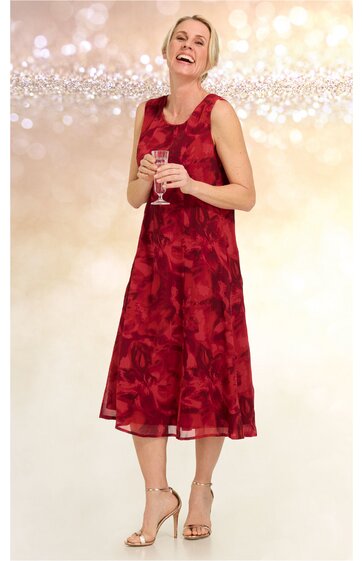 Ärmelloses midikleid in dunkelrot mit floralem Muster, rundhals, ausgestellter schwingender Rock, getragen von lächelnder frau in aufrechter stehender pose, kombiniert mit goldfarbenen offenen hohen Sandaletten