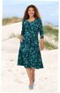Knielanges, dunkelgrünes Kleid mit blau-grünem Blattmuster, 3/4-Ärmel, Rundhalsausschnitt, zwei seitliche Eingrifftaschen, getragen von stehender Frau am Strand