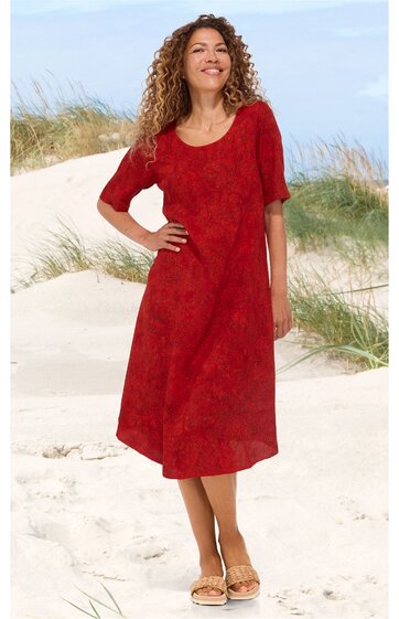 Knielanges rotes Kleid mit halbhohem Rundhalsausschnitt, kurzen Ärmeln, leicht A-förmiger Schnitt, getragen von stehender Frau am Strand mit Sanddünen im Hintergrund
