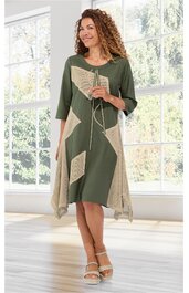 Kleid in Olivegrün mit beigen geometrischen Flächen, asymmetrischer Saum, dreiviertelärmlig, Rundhalsausschnitt mit Kordel und Quasten, getragen von stehender Frau in Innenraum vor großen Fenstern