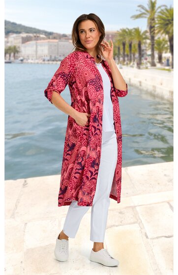 Lang geschnittener, pink-roter leichter Mantel mit abstraktem Muster, 3/4-Ärmel, offene Front, zwei seitliche Taschen, getragen von stehender Frau, kombiniert mit weißem T-Shirt, weiße Hose, weiße Sneakers