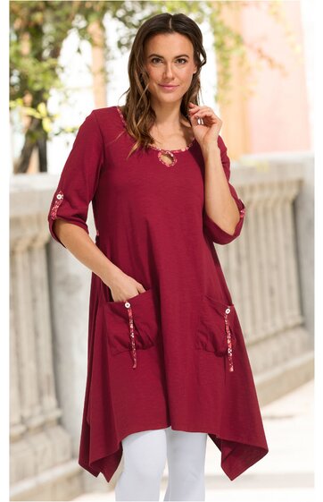 Bordeauxrotes, asymmetrisches Longshirt mit drei Viertel Ärmeln, Rundhalsausschnitt, zwei vorne aufgesetzte Taschen mit Kordelzug, getragen von stehender Frau, lockere Passform