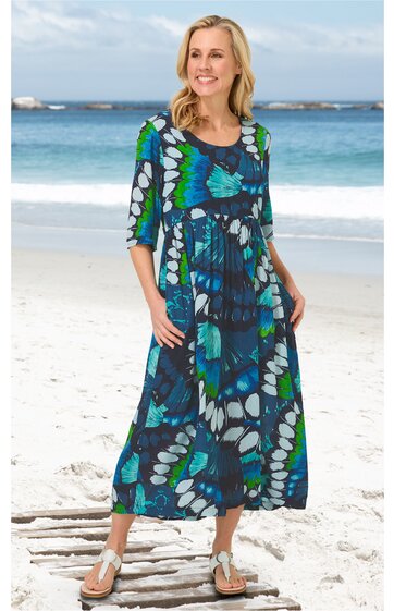 Maxikleid in Dunkelblau mit großflächigem floralen Muster in Blau, Grün und Weiß, Rundhalsausschnitt, 3/4-Ärmel, lockere Passform, ausgestellter Rock, getragen von lächelnder stehender Frau am Strand, mit Taschen