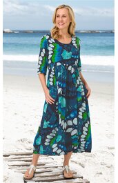 Maxikleid in Dunkelblau mit großflächigem floralen Muster in Blau, Grün und Weiß, Rundhalsausschnitt, 3/4-Ärmel, lockere Passform, ausgestellter Rock, getragen von lächelnder stehender Frau am Strand, mit Taschen