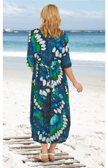 Maxikleid in Dunkelblau mit großflächigem, abstrahiertem Schmetterlingsmuster in Grün, Weiß und Türkis, halblange Ärmel, tailliert mit Tunnelzug, geraffte Rückseite, getragen von rückwärts stehender Person am Strand, leichte Stoffführung