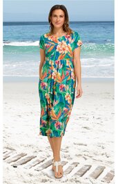 Türkisfarbenes, knielanges Kleid mit buntem Blumen- und Blattmuster, kurzer Ärmel, Rundhals, tailliert, getragen von stehender Frau am Strand, mit seitlichen Eingrifftaschen, legere Passform