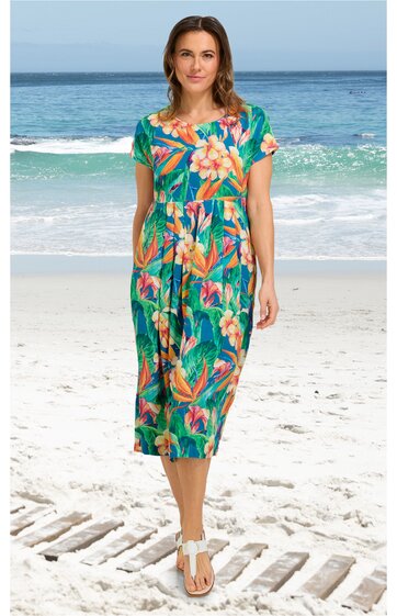 Türkisfarbenes, knielanges Kleid mit buntem Blumen- und Blattmuster, kurzer Ärmel, Rundhals, tailliert, getragen von stehender Frau am Strand, mit seitlichen Eingrifftaschen, legere Passform