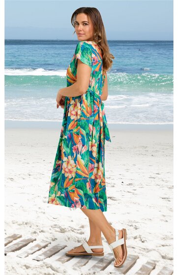 Midikleid in grün mit orange-rosa Blumenmuster, kurze Ärmel, Rundhalsausschnitt, lockere Passform, getragen von seitlich stehendem Model am Strand, Kleid reicht bis zur Wade