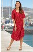 Rotes Midikleid mit floralen Muster, kurze Ärmel, runder Ausschnitt, lockere Passform, vorne rechts langer Schlitz, getragen von lächelnder stehender Frau mit offenen Haaren, weiße Sandalen