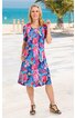Knieumspielendes Freizeitkleid in blau mit buntem Blumenmuster, rundem Ausschnitt, kurze Ärmel, zwei seitliche Taschen, locker geschnitten, getragen von stehender Frau am Strand