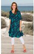 Knielanges Kleid in Petrol mit türkisfarbenem Blumenmuster, halblange Ärmel, Rundhalsausschnitt, lockere Passform, getragen von stehender Frau am Strand, kombiniert mit weißen Leggings und roten Sandalen