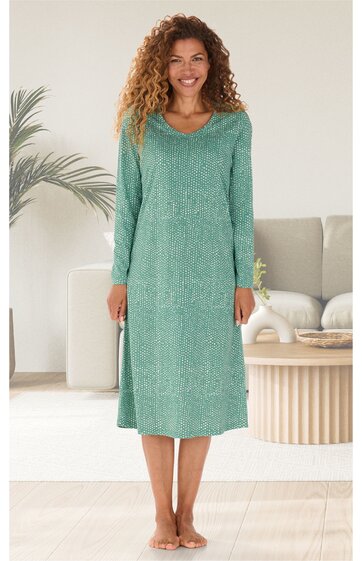 Grünes, langärmeliges Nachthemd mit rundem Ausschnitt, knielang, gerade geschnitten, getragen von stehender Frau in hellem Wohnzimmer