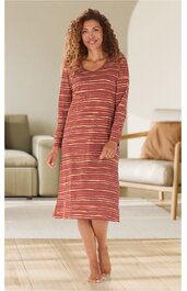 Rostorange Kleid mit buntem Streifenmuster, langärmlig, rundem Ausschnitt, midi lang, gerade geschnitten, getragen von stehender Frau mit losen Locken