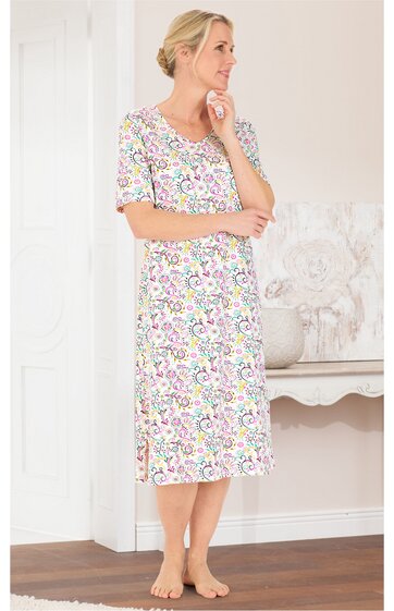 Kleid in Weiß mit buntem Blumendesign, rundem Ausschnitt, halblange Ärmel, knielang, Seitenschlitze, getragen von stehender Frau mit hochgestecktem blonden Haar