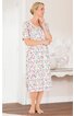 Kleid in Weiß mit buntem Blumendesign, rundem Ausschnitt, halblange Ärmel, knielang, Seitenschlitze, getragen von stehender Frau mit hochgestecktem blonden Haar