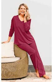 Dunkelrosa Schlafanzug mit langärmligem V-Ausschnitt-Oberteil und langen Hosen, getragen von sitzender Frau, entspannt, einfarbig, elastischer Bund an der Hose