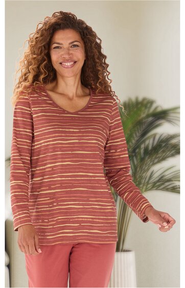 Langärmliges Pullover-Shirt in rostrot mit hellbeigen, horizontalen Streifen, V-Ausschnitt, locker sitzend, getragen von lächelnder stehender Frau, Unterteil in ziegelrot