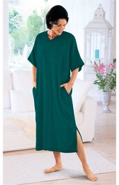 Locker fallendes, langes Kleid in dunkelgrün, ohne Muster, mit kurzen weiten Ärmeln, Rundhalsausschnitt, seitlichen Eingrifftaschen, getragen von stehender Frau, knöchellang