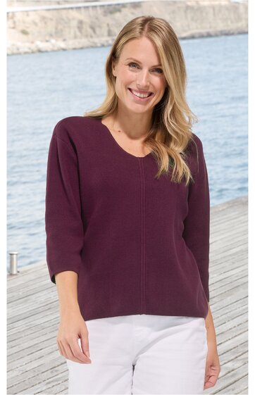 Damenpullover in dunklem Lila, einfarbig, Rundhalsausschnitt, lange Ärmel, gerade geschnitten, getragen von stehender Frau vor Wasser und Holzsteg