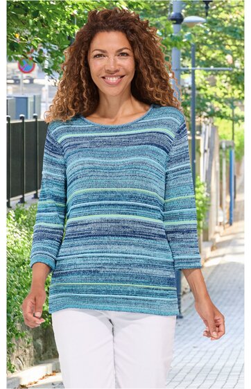 Pullover in verschiedenen Blautönen mit horizontalem Streifendesign, Rundhalsausschnitt, lange Ärmel, locker sitzend, getragen von stehender Frau im Freien