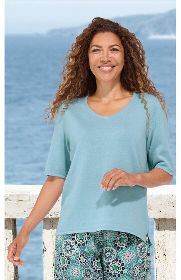 Hellblauer Pullover mit V-Ausschnitt, halblangen Ärmeln, gerade Form, getragen von lächelnder Frau vor Meereskulisse, locker sitzend