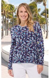 Langärmeliges Oberteil in Blau und Violett mit abstraktem Muster, rundem Kragen, gerade geschnitten, getragen von stehender lächelnder Frau vor Palmenkulisse