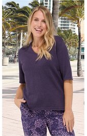 Dunkellila Kurzarmshirt ohne Muster, Rundhalsausschnitt, gerade geschnitten, getragen von stehender lächelnder Frau mit langen blonden Haaren, rechte Hand in Hosentasche