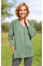 Langer, hellgrüner Strickcardigan, V-Ausschnitt, durchgehende Knopfleiste mit kleinen Knöpfen, zwei Taschen vorne, getragen von lächelnder Frau mit kurzen blonden Haaren im Freien