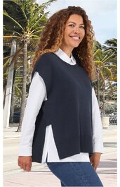 Dunkelblaue, ärmellose Weste mit seitlichen Schlitzen, rundem Ausschnitt, über weißem Langarmshirt getragen, getragen von lächelnder stehender Frau mit lockigem Haar vor Palmenkulisse