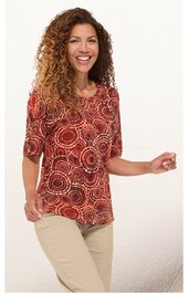 Rotes Damenoberteil mit kreisförmigem Muster in Beige und Braun, rundem Ausschnitt, halblangen Ärmeln, gerade geschnitten, getragen von stehender Frau mit lockigen Haaren