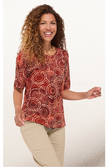 Rotes Damenoberteil mit kreisförmigem Muster in Beige und Braun, rundem Ausschnitt, halblangen Ärmeln, gerade geschnitten, getragen von stehender Frau mit lockigen Haaren